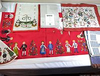 Overview of red tablecloth, runner, floral cloth, folded grey cloth and striped towel