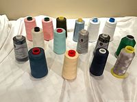 Sixteen thread cones arranged on white surface showing assorted colours