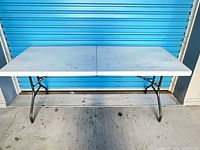 Full view of white plastic folding table with metal legs unfolded