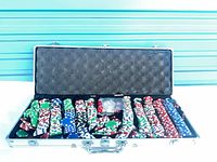 Open aluminum case showing poker chips in various colours, dice and playing cards