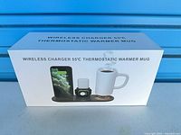 Front of product box showing wireless charger with phone, earbuds, watch and mug warmer
