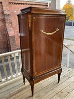 Front view of tall wooden cupboard with brass garland pull and corner mounts