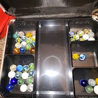 Open cash box showing compartments filled with assorted glass marbles