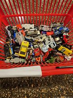 Top-down view of red basket filled with assorted Hot Wheels and Matchbox die-cast cars and trucks