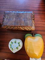 Three closed trinket boxes—wood-look ceramic, yellow apple, heart with flowers—on tabletop