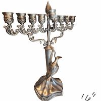 Front view of silver-tone nine-branch menorah showing scroll arms, candle cups, shamash, pitcher ornament, base