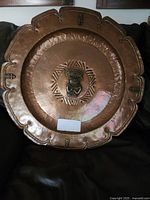 Front view of large hammered copper plate showing scalloped edge and central Mayan medallion