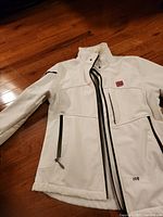 Front view of white softshell coat showing flag patch and zippers