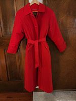 Front view of red trench coat on hanger showing full length and belt