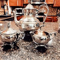 Full view of silver plated teapot, sugar bowl with lid, and creamer on countertop
