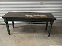 Full view of bench showing green legs and worn charcoal laminate top