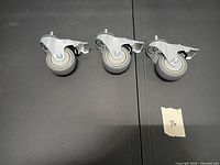 Three heavy duty swivel casters laid out on surface showing wheels and brake levers
