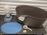 Litter box, water dispenser, placemat, scoop grouped together