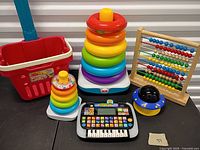 Group shot of oversized and classic Rock-a-Stack, VTech keyboard, wooden abacus, red shopping basket, star projector
