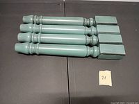 Four teal painted turned wood legs with square tops laid side by side