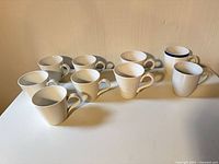 Nine assorted white ceramic mugs on table