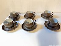 Six Denby Greystone cups on saucers arranged on table
