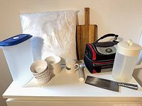 Group shot of all items: cushion insert, lunch bag, cutting board, cleaver, containers, ramekins, sugar shaker, scoop