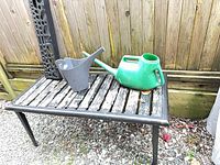 Cast iron table with wooden slats, green watering can, grey watering can
