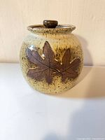 Front of speckled stoneware jar showing maple leaf appliques and lid