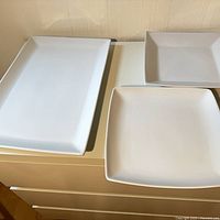 Three white ceramic platters on surface, one rectangular and two square