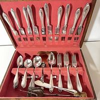 Open flatware chest showing assorted forks, spoons, serving pieces