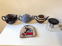 All four teapots and beaded tea cosy shown together
