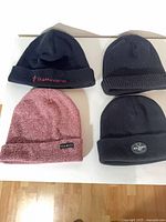 Four knit beanies laid out: black Baffinland, black rib-knit, maroon YEA.NICE, black with round patch
