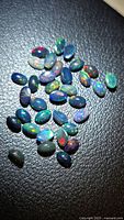 Group of oval black opal cabochons on dark surface