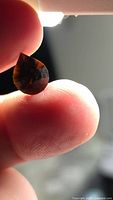 Pear-cut deep orange tourmaline held between fingers
