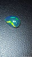 Pear cabochon opal showing green and blue flashes on dark background