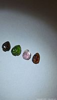 Four differently colored leaf-cut tourmaline gems on light background
