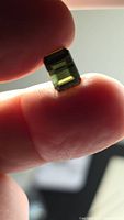 Front view of rectangular green tourmaline held between fingers