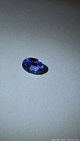 Loose oval blue-purple tanzanite on neutral background, angled to show facets