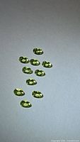 Front view of ten apple green oval peridot gemstones on light background
