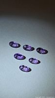 Six oval purple amethysts arranged on flat surface