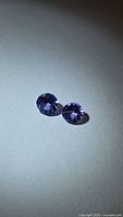 Pair of round purple-blue gemstones under direct light
