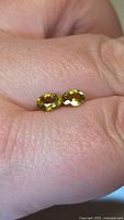 Two oval yellow-green faceted sphene gemstones on fingers