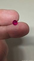 Round vivid red ruby held between fingers