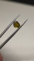 Heart-cut yellow-green tourmaline held by tweezers