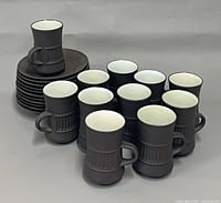 Group of 11 mugs in front of stacked saucers