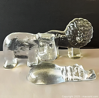 Group shot of three clear glass animal figurines (lion, standing hippo, reclining hippo)