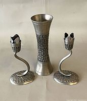 Front view of pewter vase flanked by two candle holders