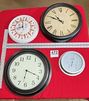 Overall view of three clocks and one weather instrument with rulers for scale