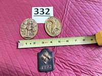 Two brass ovals and one black cast-iron shield fire mark with tape measure for scale