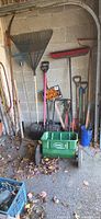 Wide view of assorted long-handled yard tools and Scotts spreader