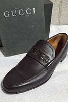 Left shoe angled view showing leather texture, strap detail, and Gucci box in background