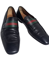 Pair of black Gucci loafers angled view showing web strap and overall condition
