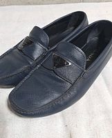 Top angled view of both blue Prada loafers showing saffiano texture and logo