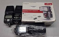 Front view of two Nikon flashes, Metz box, Metz flash in plastic